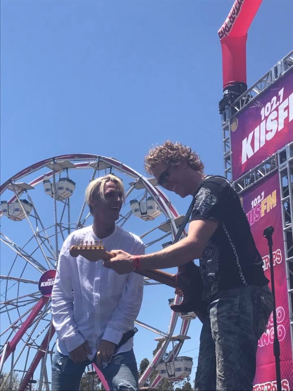 Aaron Carter laughing as Erik shows him the guitar, ferris wheel behind them at Wango Tango