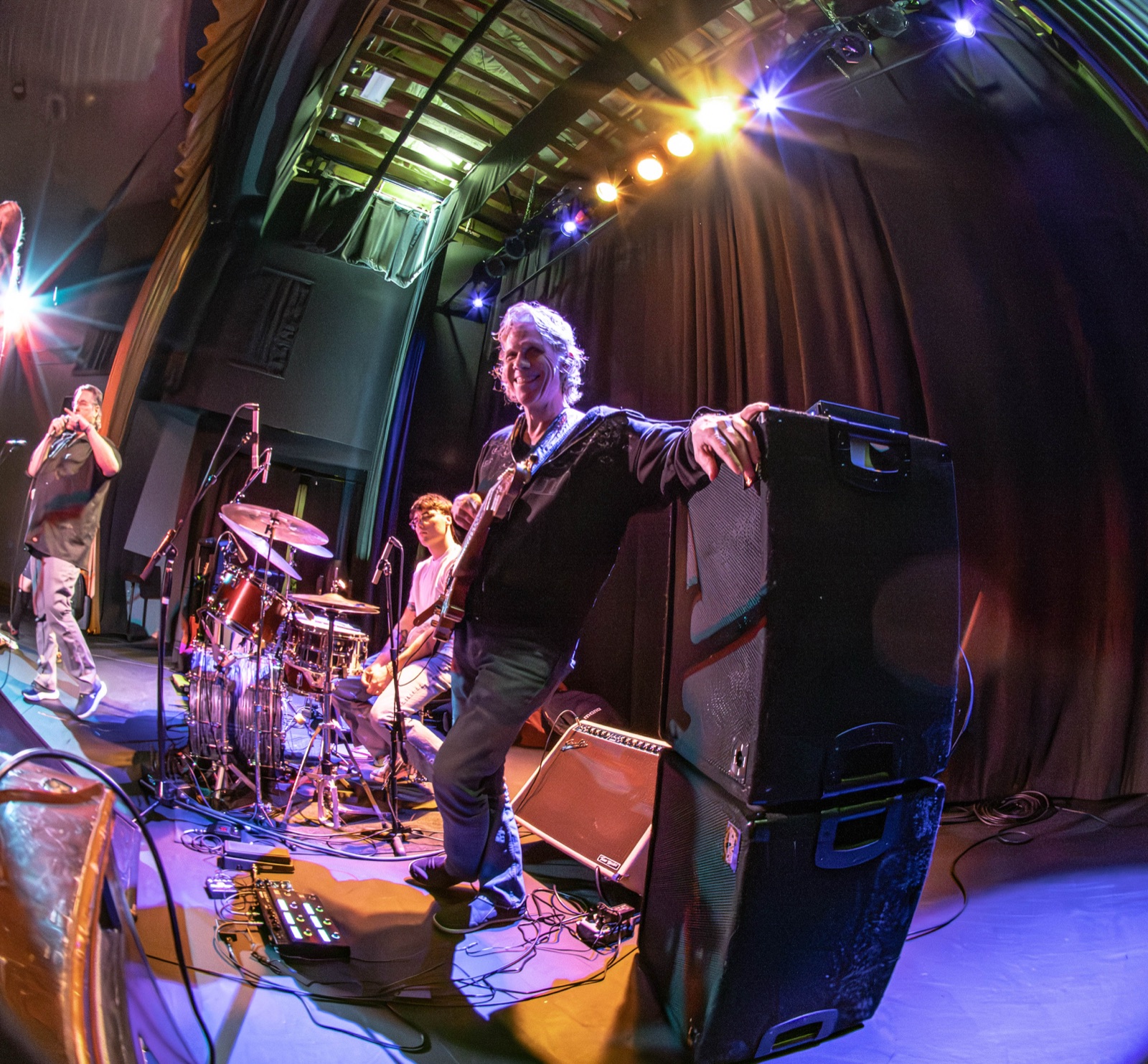 Fisheye shot of Erik with arm slung over an amp stack, grinning