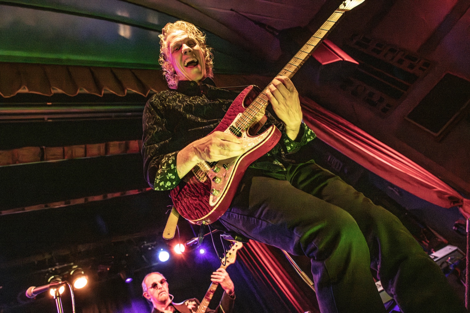 Extreme low-angle fisheye of Erik leaning way back in a green suit, magenta-red room